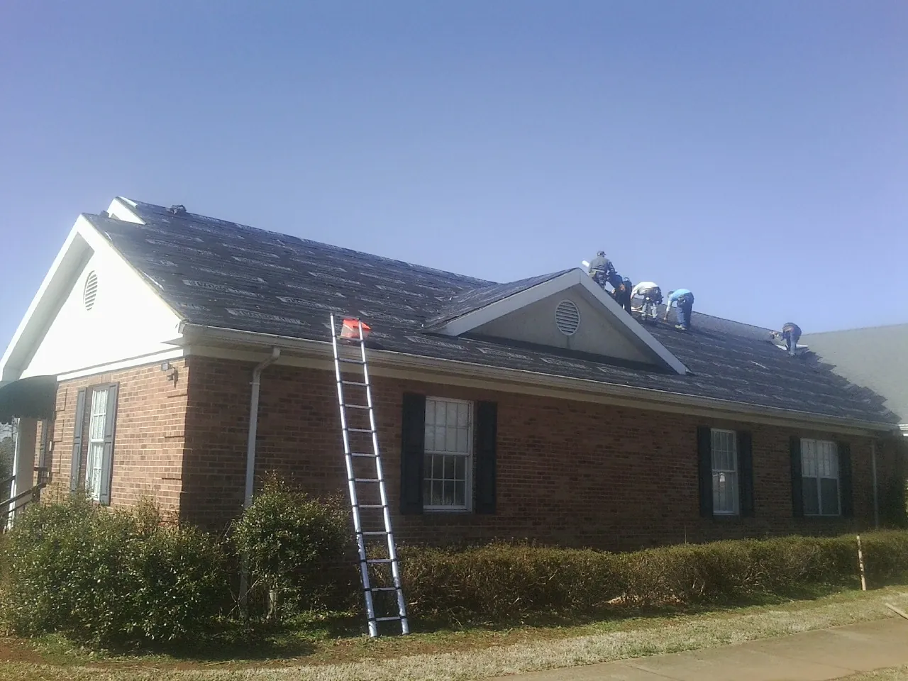 Crew tearing shingles off a brick ranch roof with a ladder set — Emergency Roof Repair work by our crew in Elizabeth
